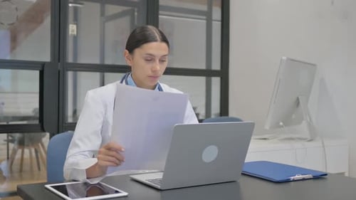 Female Doctor Doing Paperwork with Laptop