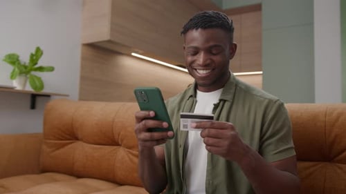 Smiling Man Using Phone and Credit Card at Home