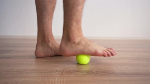 Man Rolls Foot Over Tennis Ball for Massage