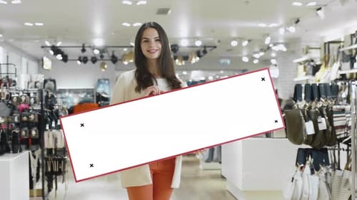 Young smiling brunette woman is holding a blank mock-up sign in a department store.
