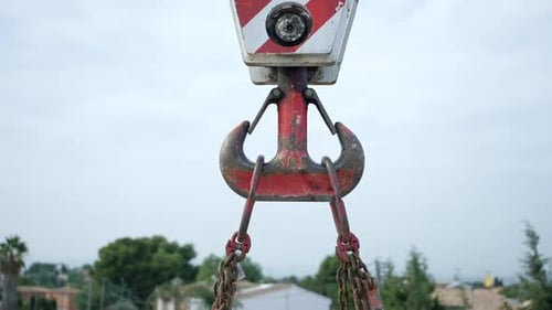 Strong steel chained crane pulley with weathered red paint lifting heavy equipment