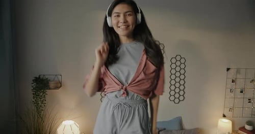 Portrait of Attractive Asian Girl in Pajamas Dancing and Singing Listening to Music with Headphones