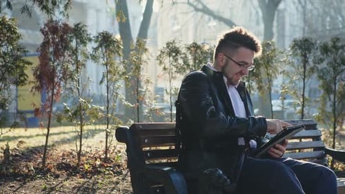 Man Sitting on Bench Using Tablet in Park