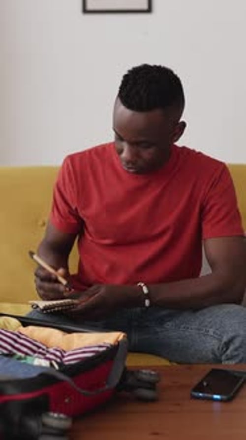 Man Packing Suitcase and Writing in Notebook