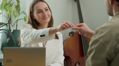 A Smiling Female Real Estate Agent Hands the Keys to a Man Buying a House a Client Becomes the Owner