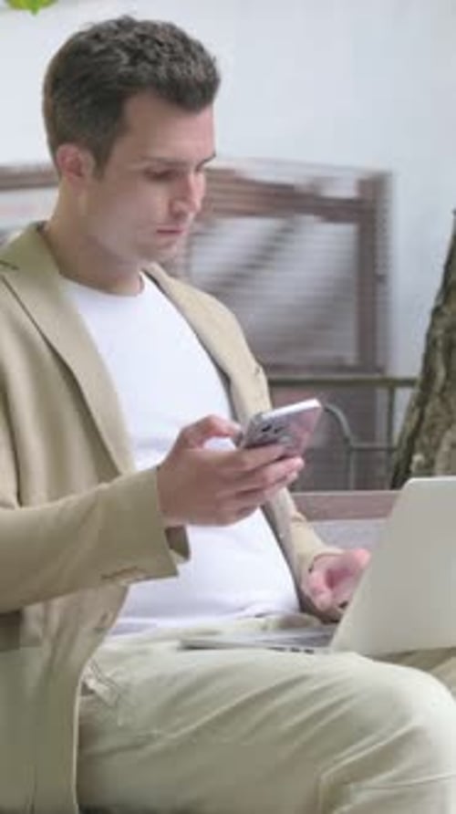 Man Sitting Outside Using Phone and Laptop