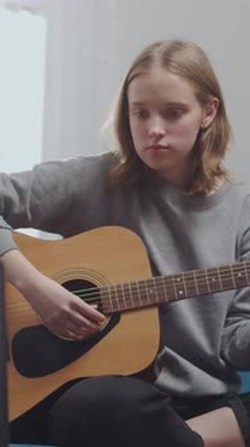 Teen Girl Practicing Acoustic Guitar at Home While Following Online Lesson on Laptop Focused