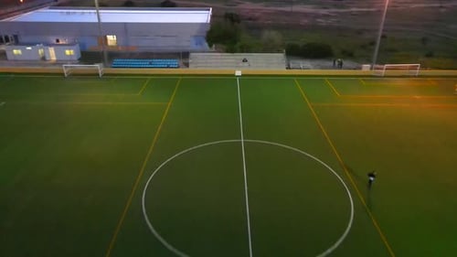Backwards revealing drone shot of a football field during golden hour flying over the middle line in