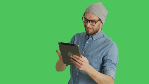 Mid Shot of a Stylish Man Wearing Hat and Glasses Using Tablet Computer. Background is Green Screen