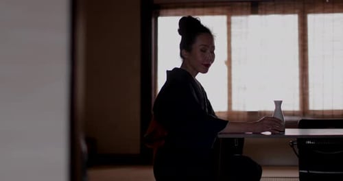Mujer japonesa con kimono junto a la ventana tradicional bebiendo Saki, Kioto, Japón