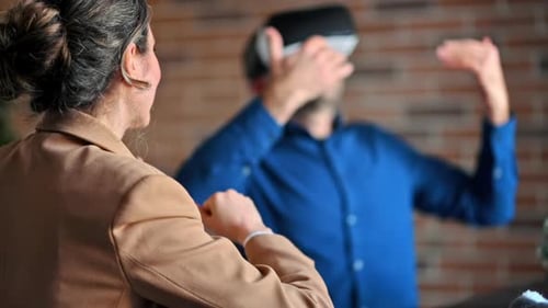Man using a Virtual Reality headset in an office while woman explains and gesticulates