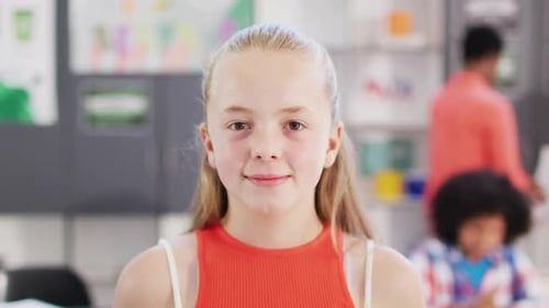 Portrait of happy caucasian schoolgirl at desk in school classroom