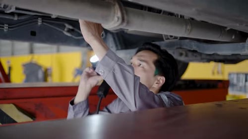 Car Mechanic Inspecting Vehicle With Flashlight