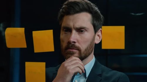 Thoughtful Man Looking at Sticky Notes in Office
