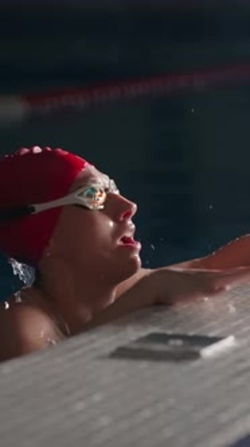 Focused Female Swimmer in Red Swim Cap Reaching the Pool Edge After Intense Lap Catching Breath with
