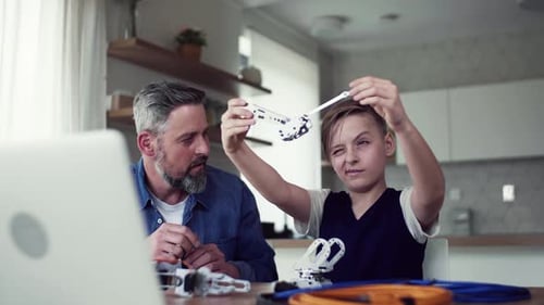 Mature Father with Small Son Sitting at Table Indoors, Working on School