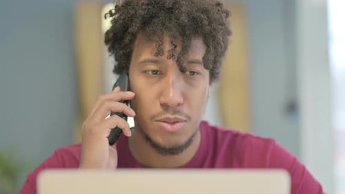 Close Up of African Man Talking on Phone while using Laptop