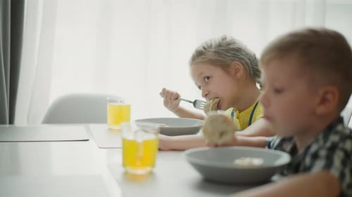 Close Up of White Children Eating Lunch at Dining Table with Bright Light
