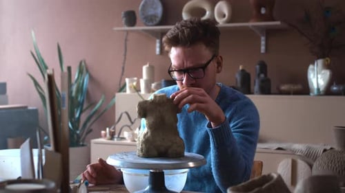 A Bearded Male Sculptor with Glasses Makes a Statue of a Female Figure A Ceramist Man Sculpts a