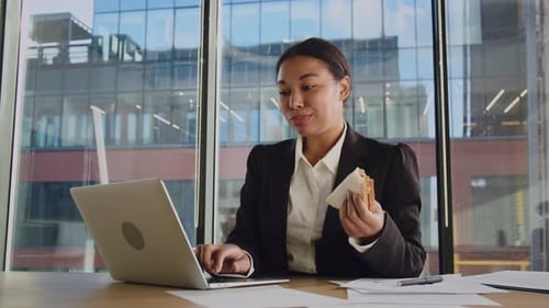 Junge afroamerikanische Frau isst bei der Arbeit Schwarze Frau im Büro isst Sandwich zum Frühstück