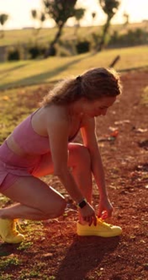 Happy young woman runner tying her sport shoes outdoors in autumn park