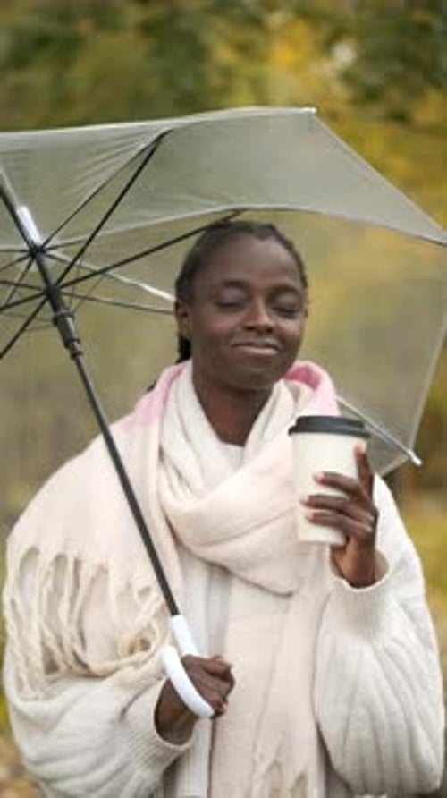 Smiling Woman Holding Coffee and Umbrella Outdoors