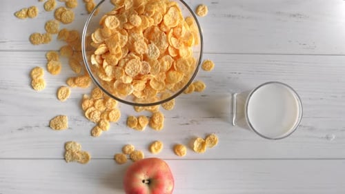 Healthy Breakfast Fresh Corn Flakes in Bowl Milk Yogurt Apple on Wooden Table Top View Tracking Shot