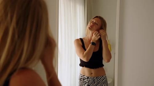 Woman Adjusting Earrings in Front of Mirror