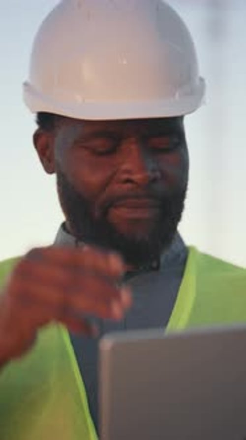 Bearded Foreman Viewing Drawings on Display of Modern Laptop in Construction Site Vertical Portrait