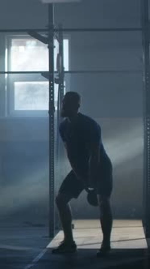 Silhouetted Athlete Performing Intense Kettlebell Swings in a Dimly Lit Gym Training Strength and