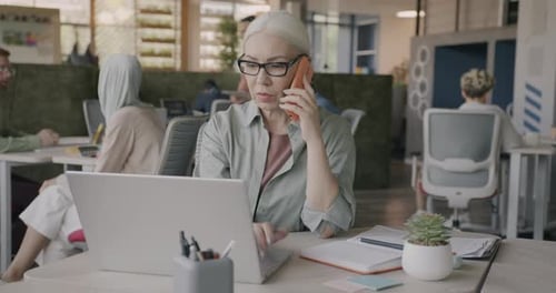 Senior Woman Works on Laptop, Talks on Phone