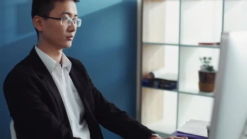 Un joven chino serio con gafas usa una computadora para mirar la pantalla en un negocio de oficina