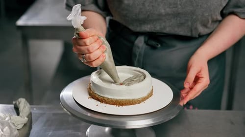 Close Up Female Baker in a Professional Kitchen Puts Cream From Pastry Bag Onto a Sponge Cake