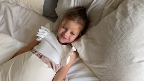 Smiling Girl Lies in Bed Underneath Grey Blanket