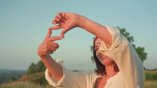 Woman Framing Sunset with Hands in Rural Setting