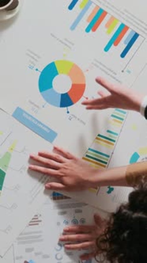 Vertical of Woman and Man Analysing Colourful Graphs Pointing at Papers