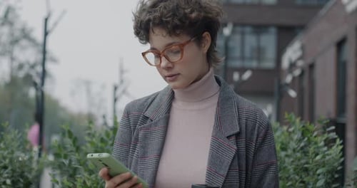 Young Businesswoman Messaging with Smartphone Standing Outdoors in Urban Street Holding Coffee Cup