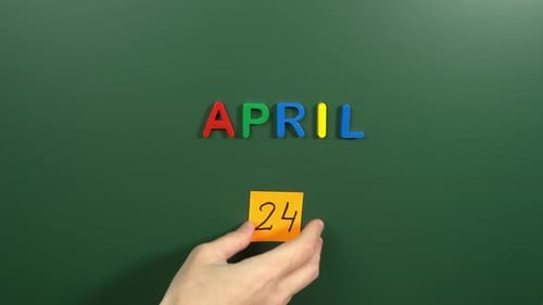 Hand sticking a sticker 24 April calendar day on school board. 24 date of April. Twenty fourth day