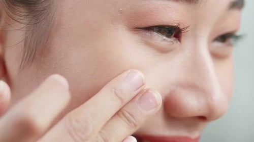 Close Up Of Beautiful Young Asian Woman Applying Face Cream And Smiling While Wearing Makeup