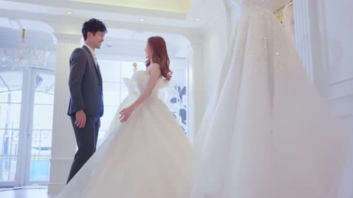 Asian beautiful bride trying on wedding gown with her fiance in studio.