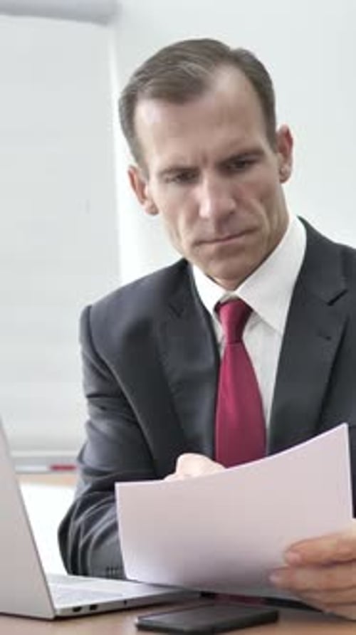Businessman Analyzing Documents with Laptop in Office