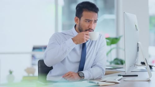 Exhausted businessman typing on a computer working and sipping coffee in a corporate office