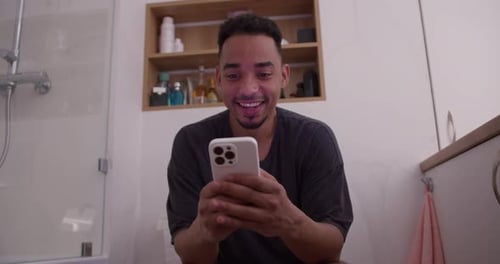 Happy Brunette Guy with a Stubble Beard with Black Skin Color in a Tshirt Holds His White Phone