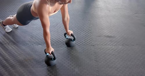 Performing push-ups with kettlebell, woman exercising in gym for fitness training, copy space