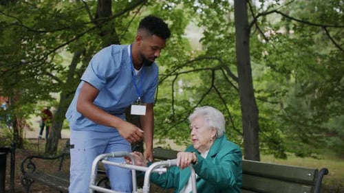 Caring african american man helps senior caucasian woman stand from park bench