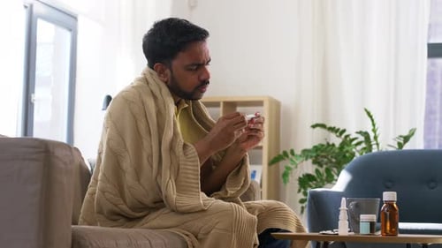 Man Wrapped in Blanket Reads Thermometer at Home
