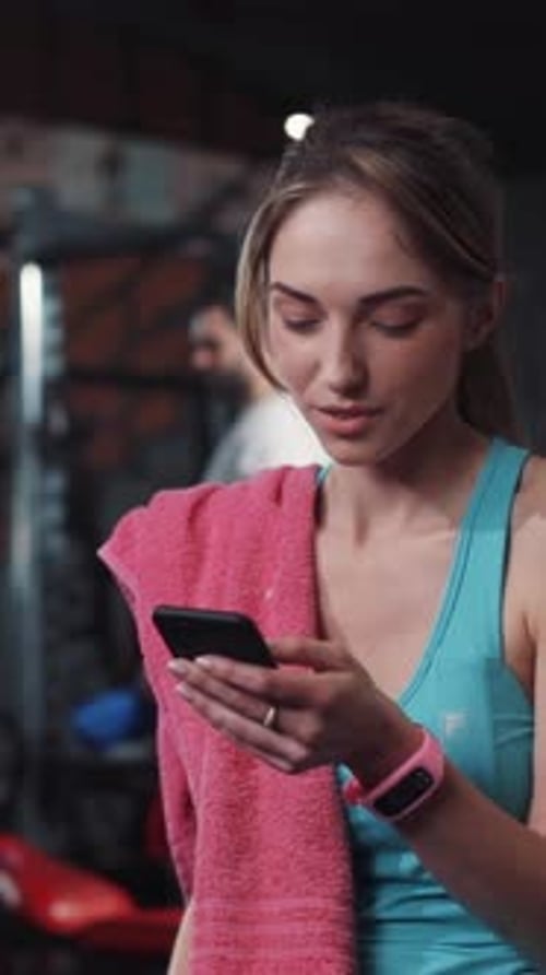 Determined and Focused Woman Utilizing Her Smartphone in a Fitness Gym Environment