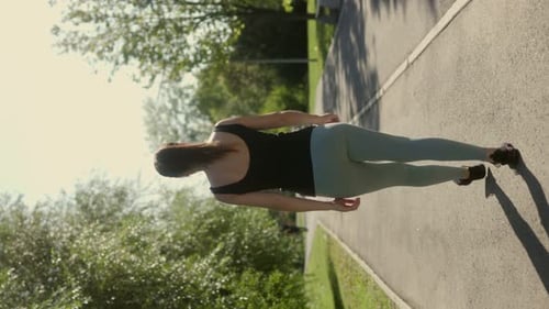 Back View of a Woman Strolling Through a Lush Green Park on a Sunny Day Vertical Shot