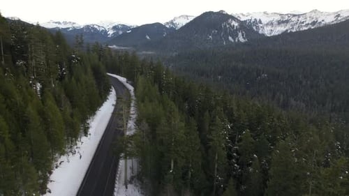 Mountain Pass in winter with light snow on ground and green pine trees- aerial ascending