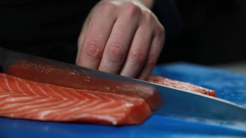 The chef slices a piece of raw salmon